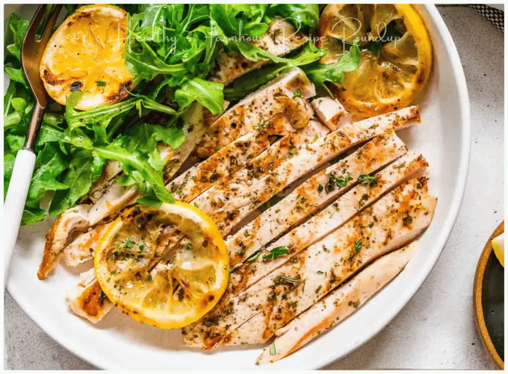 Grilled chicken breasts cut into strips on a plate with greens and lemon slices.
