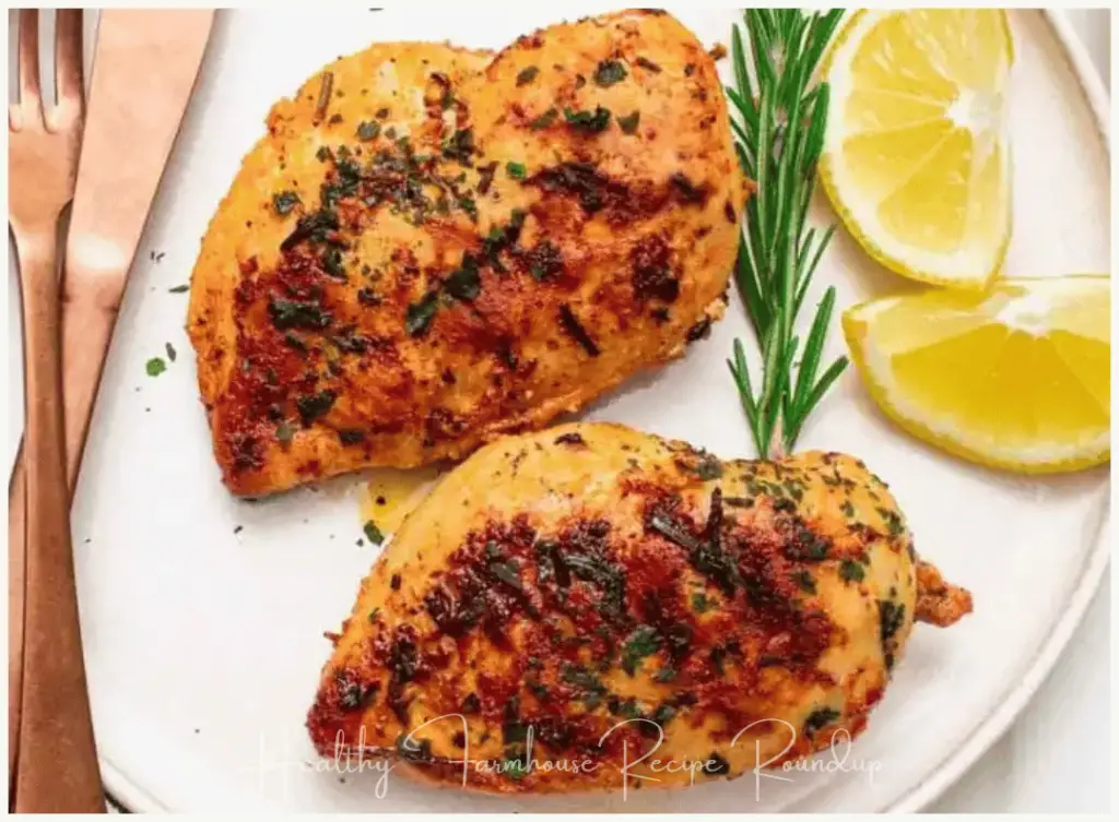 Grilled chicken breasts on a plate with rosemary sprig and lemon wedges