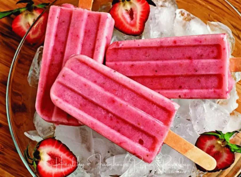 Bright pink popsicles in a bowl of ice with sliced strawberries
