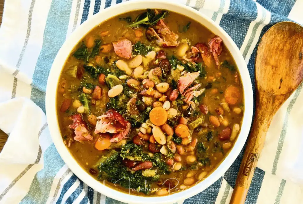 White bowl filled with a healthy bean and greens soup sitting next to a wooden spoon