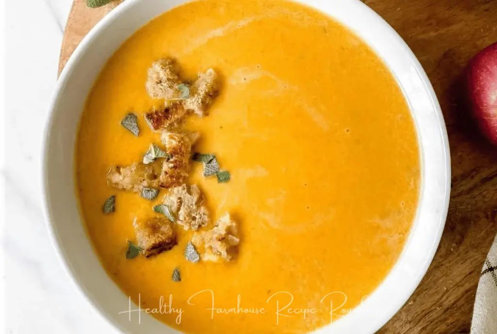 White bowl of orange colored soup and breadcrumbs