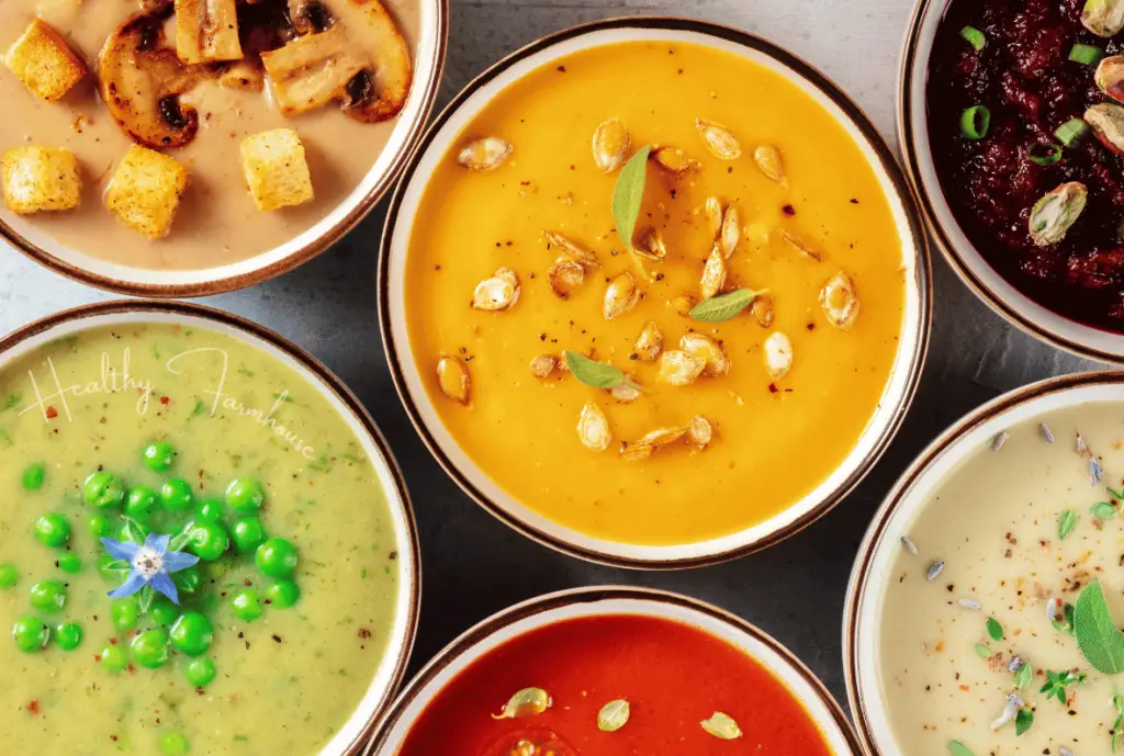 6 bowls of different healthy soup recipes - one bowl has mushrooms and croutons in a tan cream base, 1 bowl has pumpkin seeds and herbs in an orange cream base, 1 bowl of chili, 1 bowl of green pea soup topped with peas, 1 bowl of tomato soup, 1 bowl of white cream base with herbs and seasonings on top.