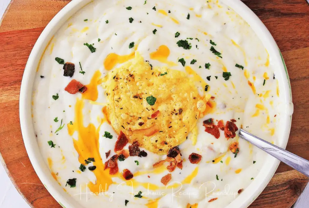 Bowl of white cauliflower healthy soup, topped with greens and bacon