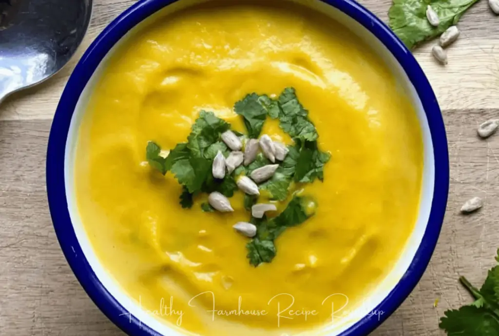 Royal blue bowl filled with bright yellow soup and topped wtih greens and sunflower seeds.