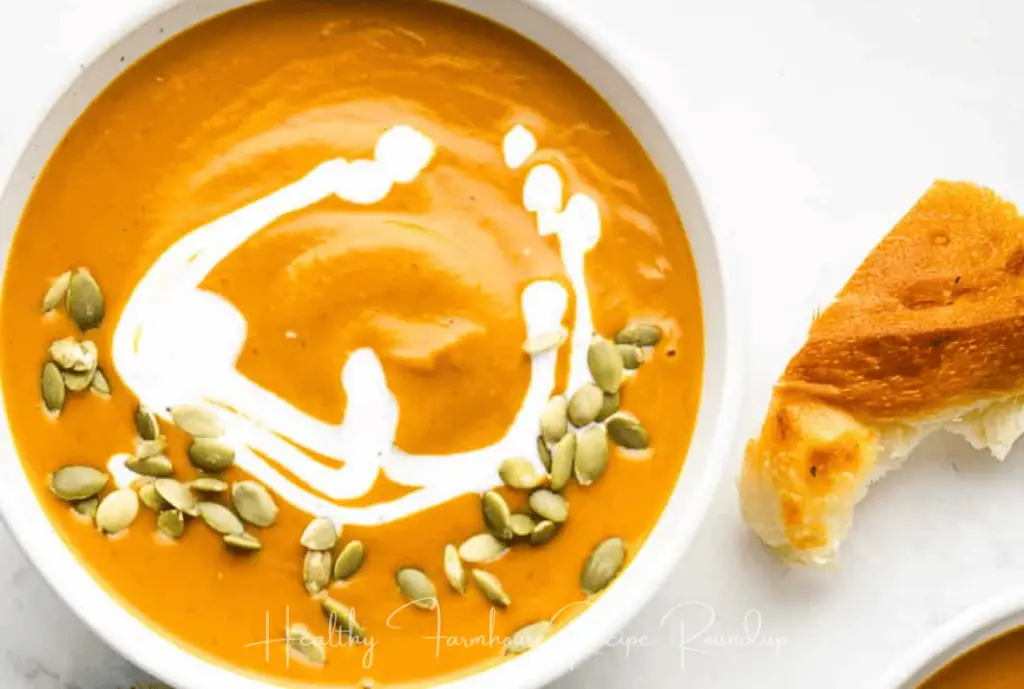 bowl of healthy pumpkin soup recipe with swirl of cream and sprinkle of pumpkin seeds on top sitting next to a piece of bread for dipping