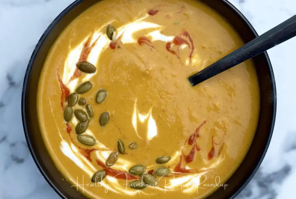 Creamy pumpkin soup recipe in black bowl with cream and pumpkin seeds on top