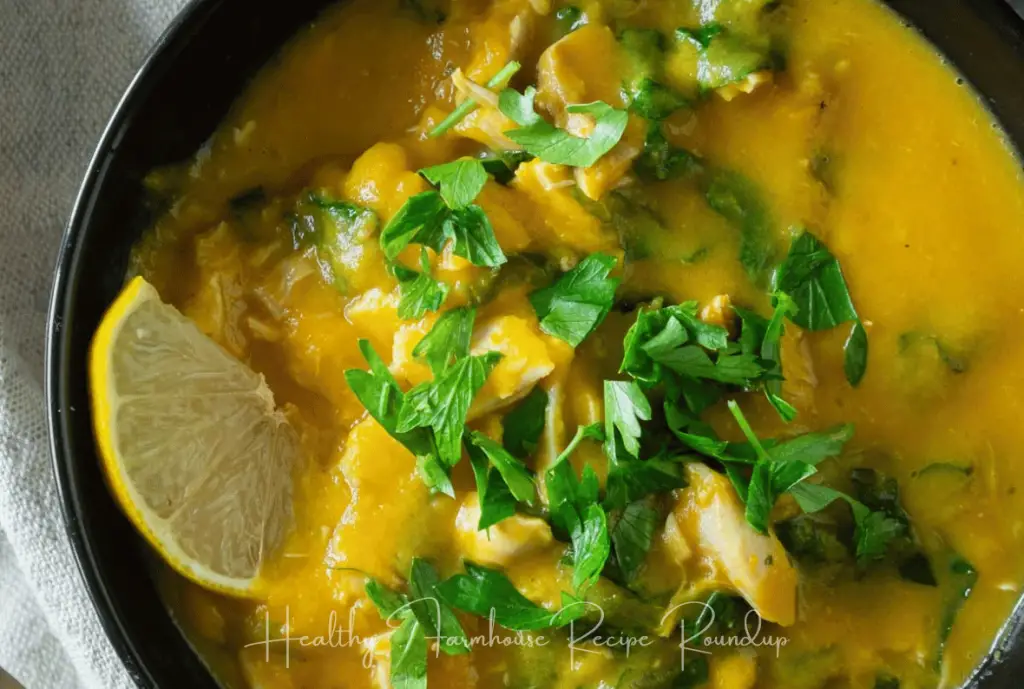 Golden glow healthy soup recipe in a black bowl and topped with herbs and a lemon wedge