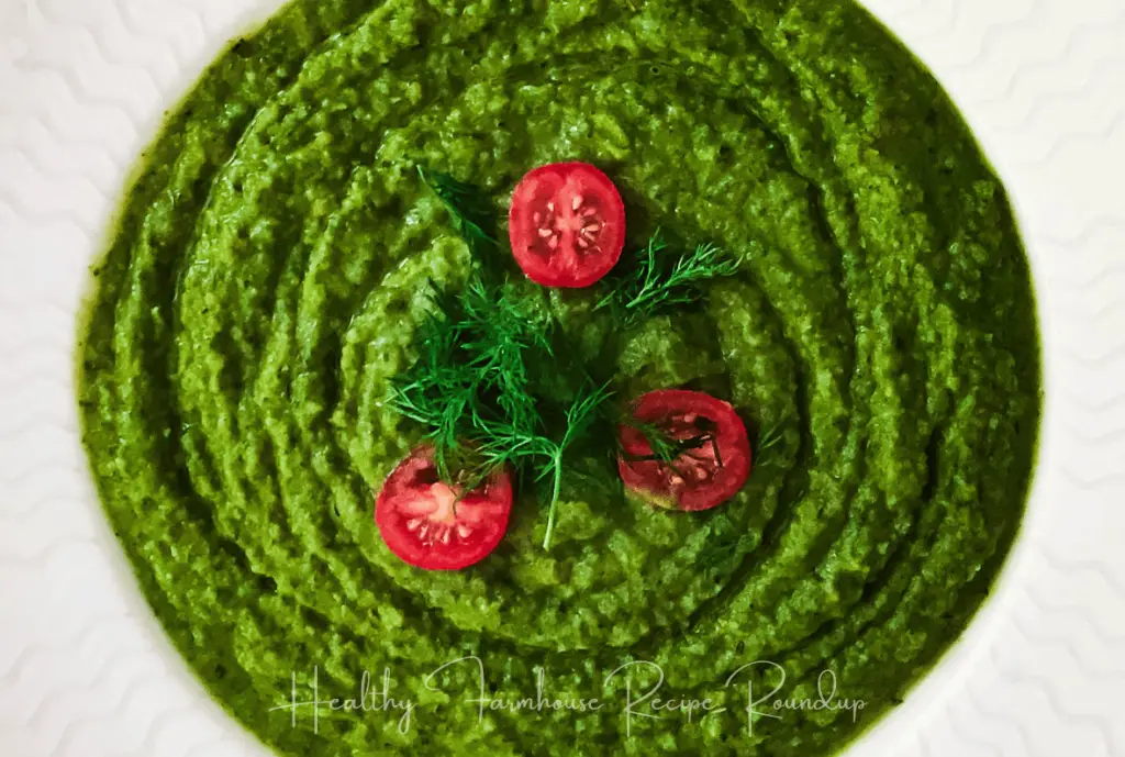 Vibrant green soup topped with halved cherry tomatoes and herbs.