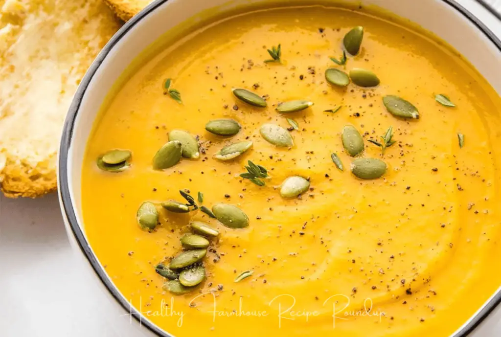 Vibrant bowl of butternut squash soup in white bowl, pumpkin seeds sprinkled on top.