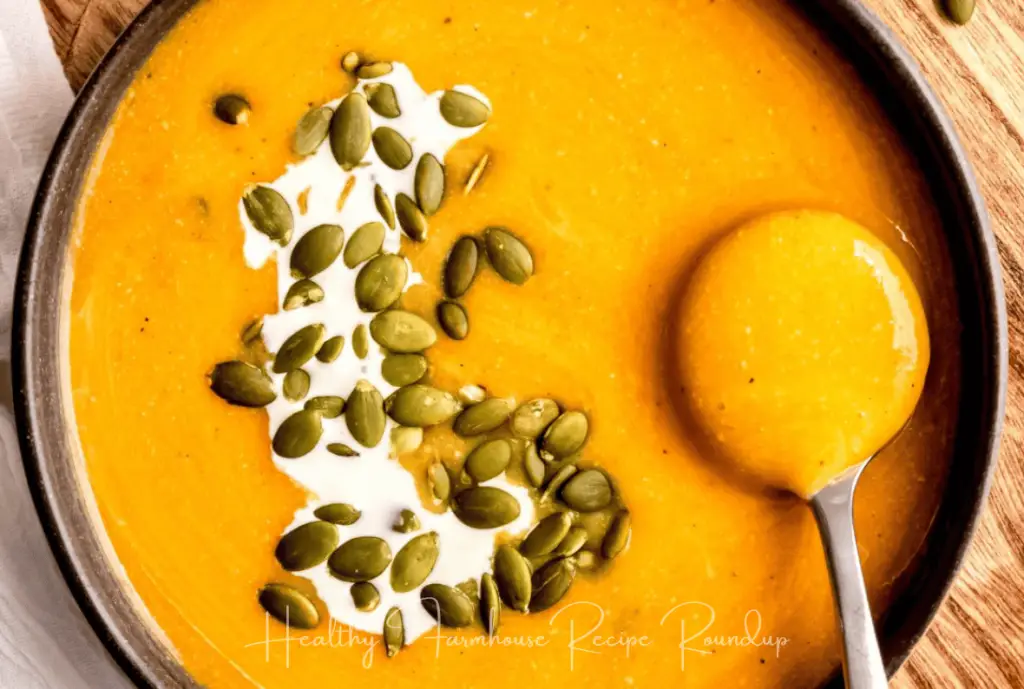 Brown bowl of creamy orange colored butternut squash soup that is topped with pumpkin seeds and a splash of cream