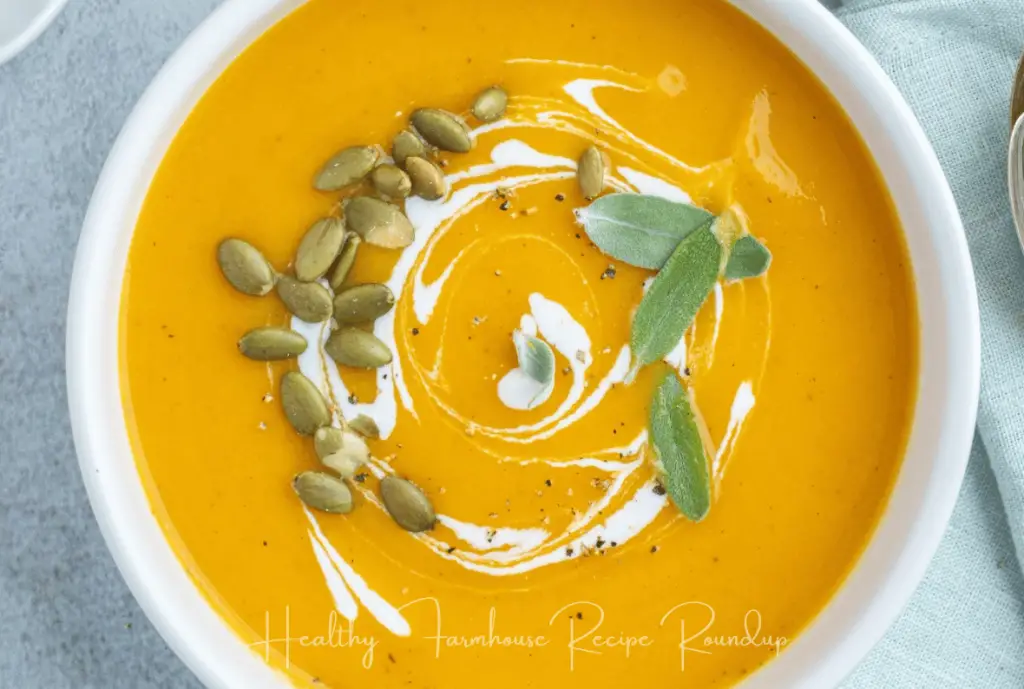 White bowl of pumpkin soup with pumpkin seeds and sage for garnish