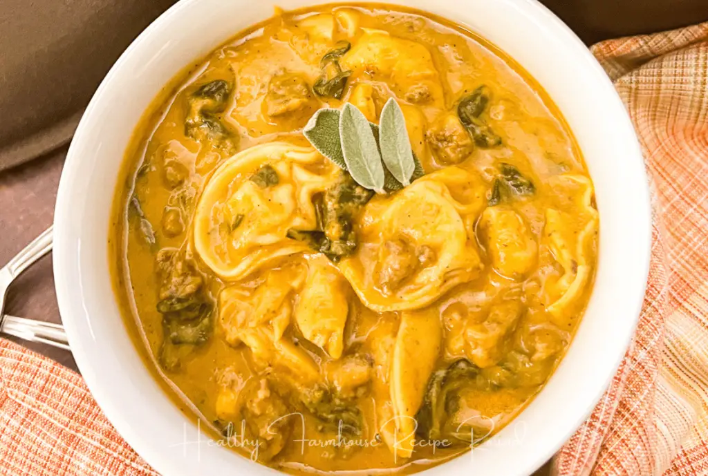 White bowl filled with tortellini soup, topped with sage leaves