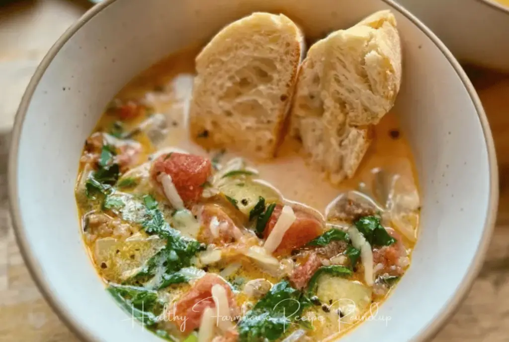 Healthy fall soup, made with greens, tomatoes, and sausage, in a white bowl with bread slices