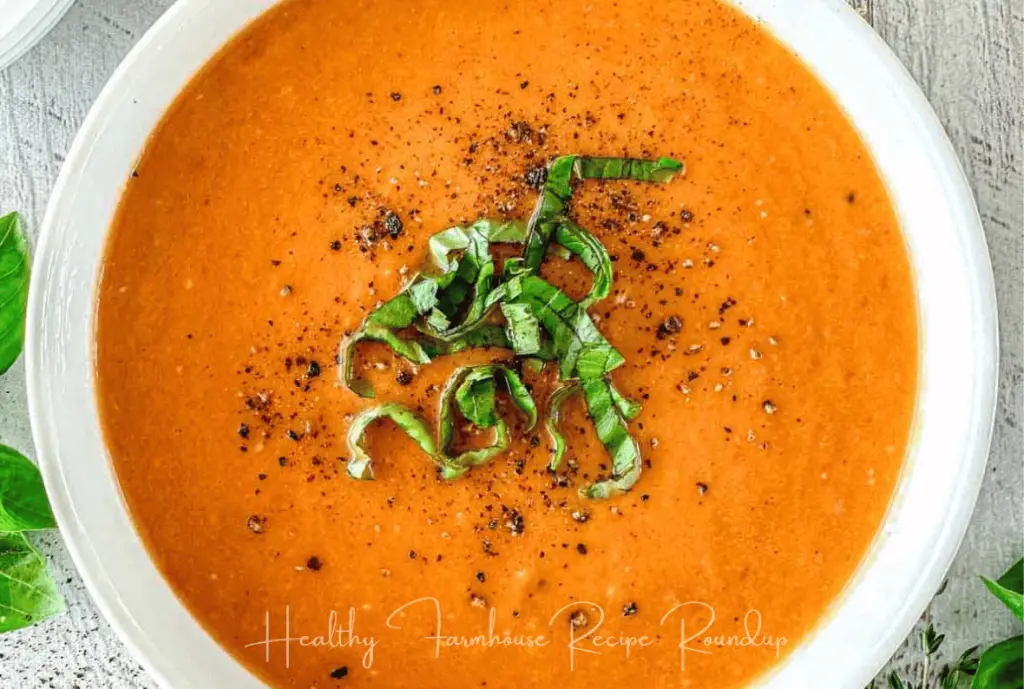 White bowl of tomato soup topped with basil