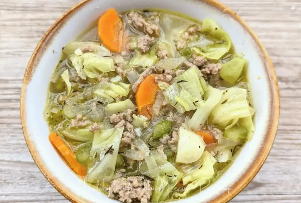 healthy fall soup made with cabbage, carrots, and sausage in a gold rimmed white bowl