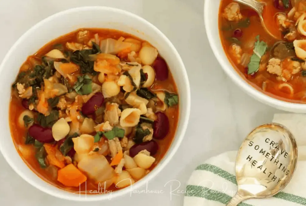 Easy vegetable fall soup recipe with red broth, veggies, greens, and pasta shells, in a white bowl. Spoon to the side with text: crave something healthy