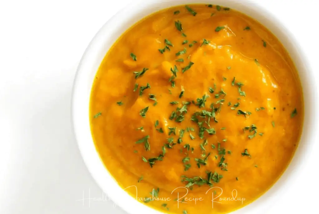 Bright orange soup in white bowl with green herbs sprinkled on top