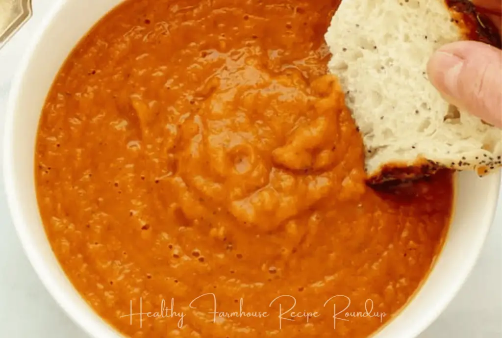 White bowl filled with red soup and a piece of crusty bread.