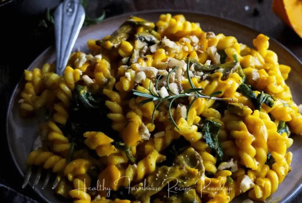 Brown plate filled with pumpkin pasta and garnished with fresh herbs