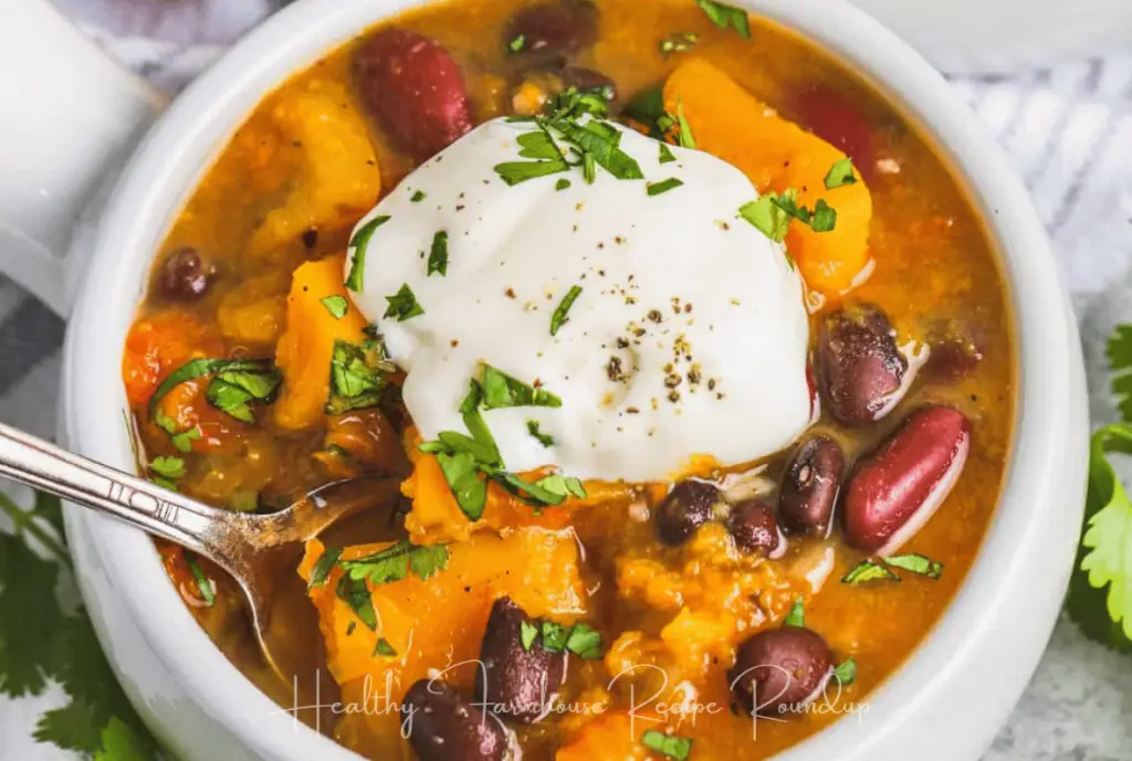 White bowl filled with butternut squash chili and topped with sour cream and herbs.