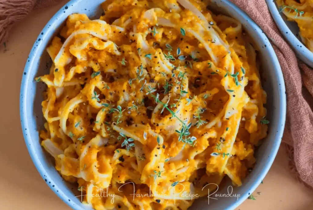 Creamy butternut pasta recipe: blue bowl filled with fettuccini noodles covered in orange butternut squash cream sauce and topped with dry herbs.