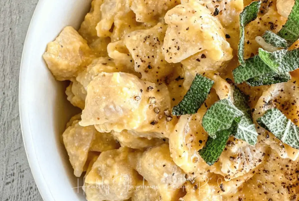 Macaroni shell pasta covered in creamy sauce, topped with pepper and herbs, served in a white dish.