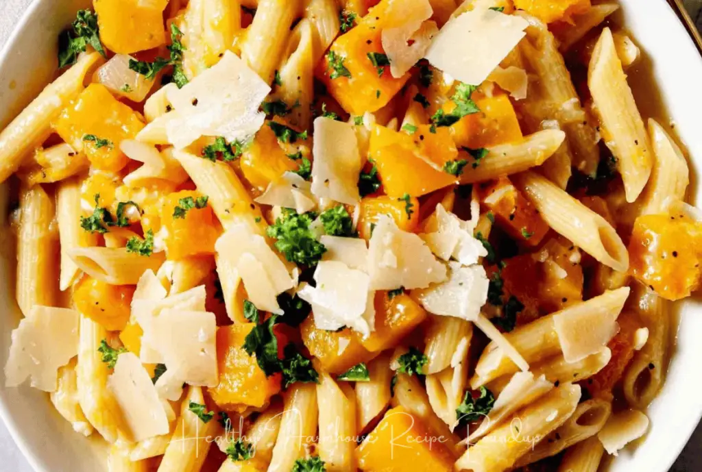 Butternut squash penne pasta sprinkled with herbs and parmesan cheese in white bowl.