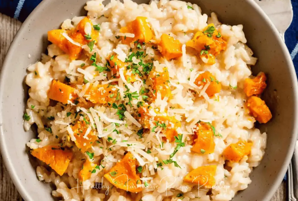 Tan bowl of rissoto topped with butternut squash cubes, shredded cheese, and herbs.