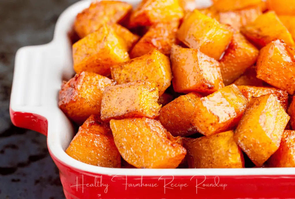 Butternut squash cut into cubes, coated in cinnamon sugar mixture, in a red baking dish.