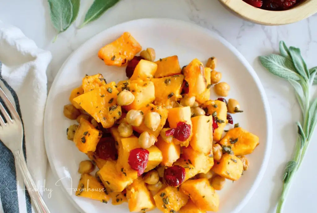 Savory chickpea butternut squash side plated on a white plate and toped with cranberries.