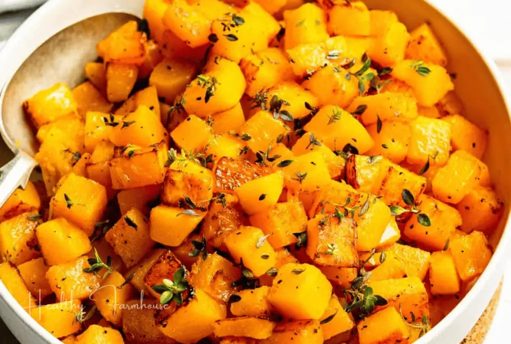 Cubes of butternut squash coated in herbs in a white bowl.