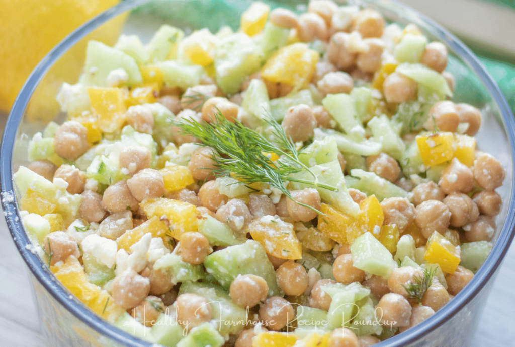 Clear bowl filled with yellow, tan, and green chunks of chickpeas, bell pepper, and cucumber with garnish on top
