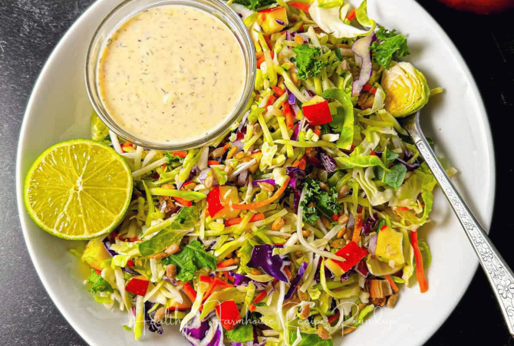 Kale slaw that looks similar to a salad in a white bowl with dressing and lime wedges on the side