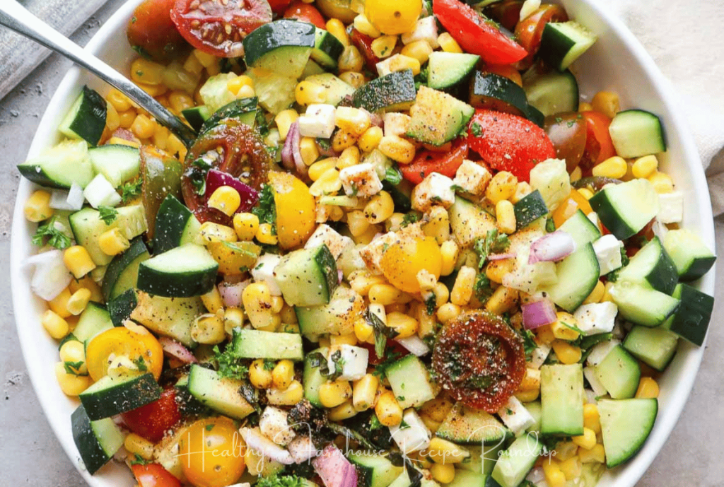 Brightly colored summer salad in a white bowl with cucumbers, tomatoes, corn, and seasonings.