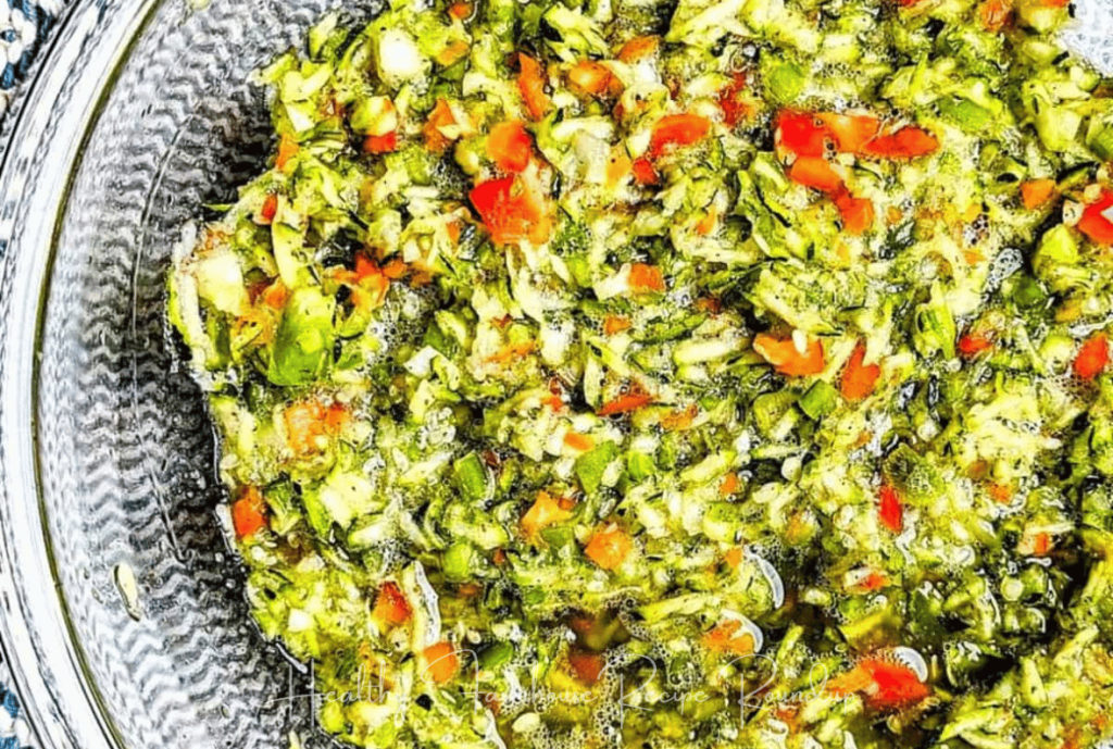 Shredded green zucchini slaw in a clear class bowl with specs of red pepper